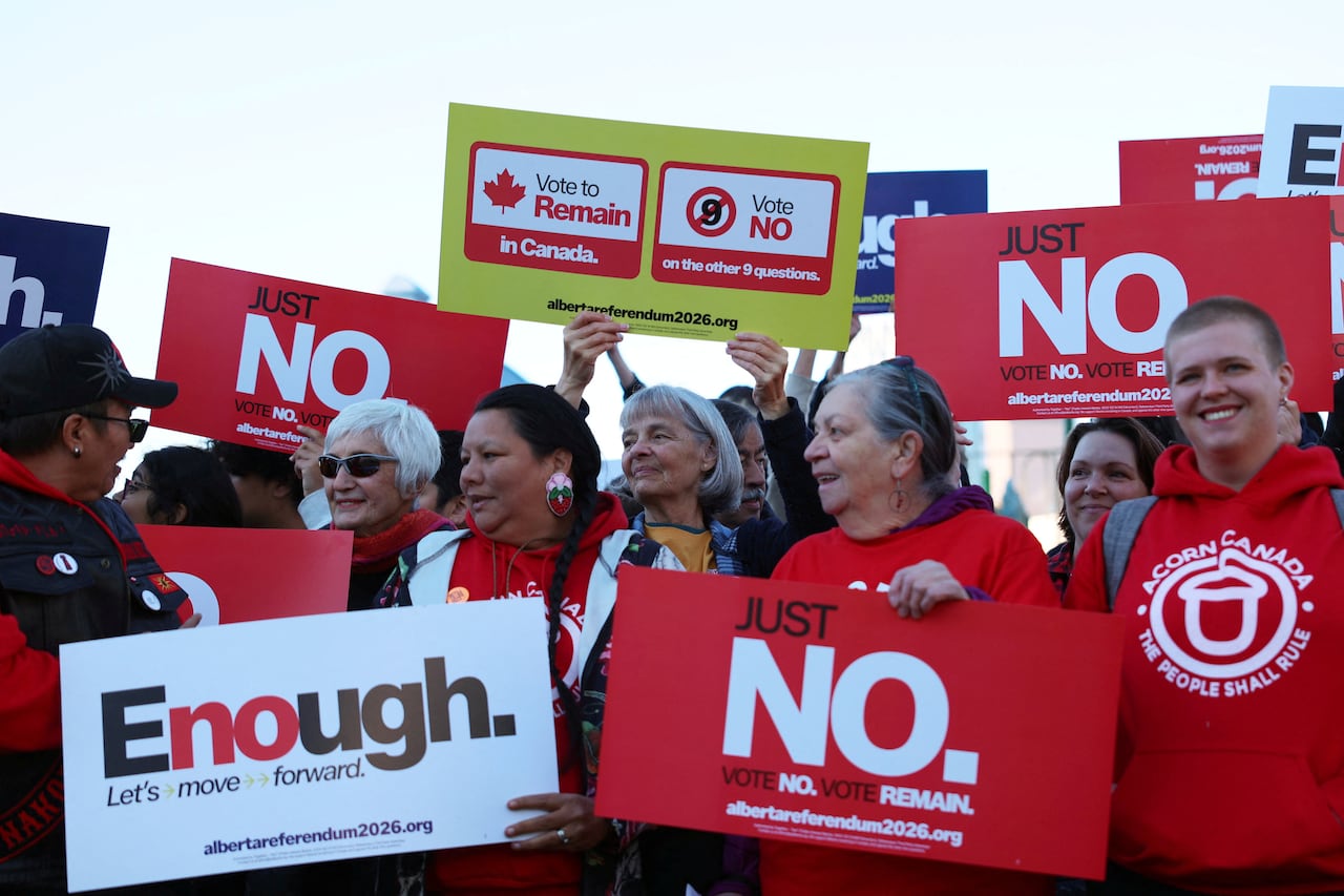 People hold up signs that oppose the Alberta referendum.