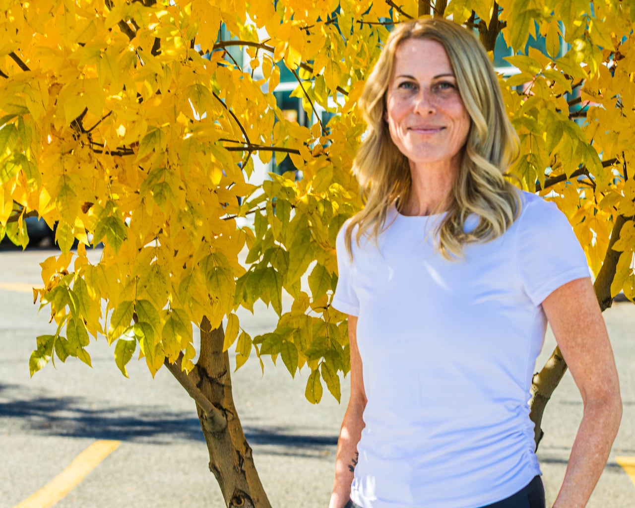 A woman stands in front of a small tree.