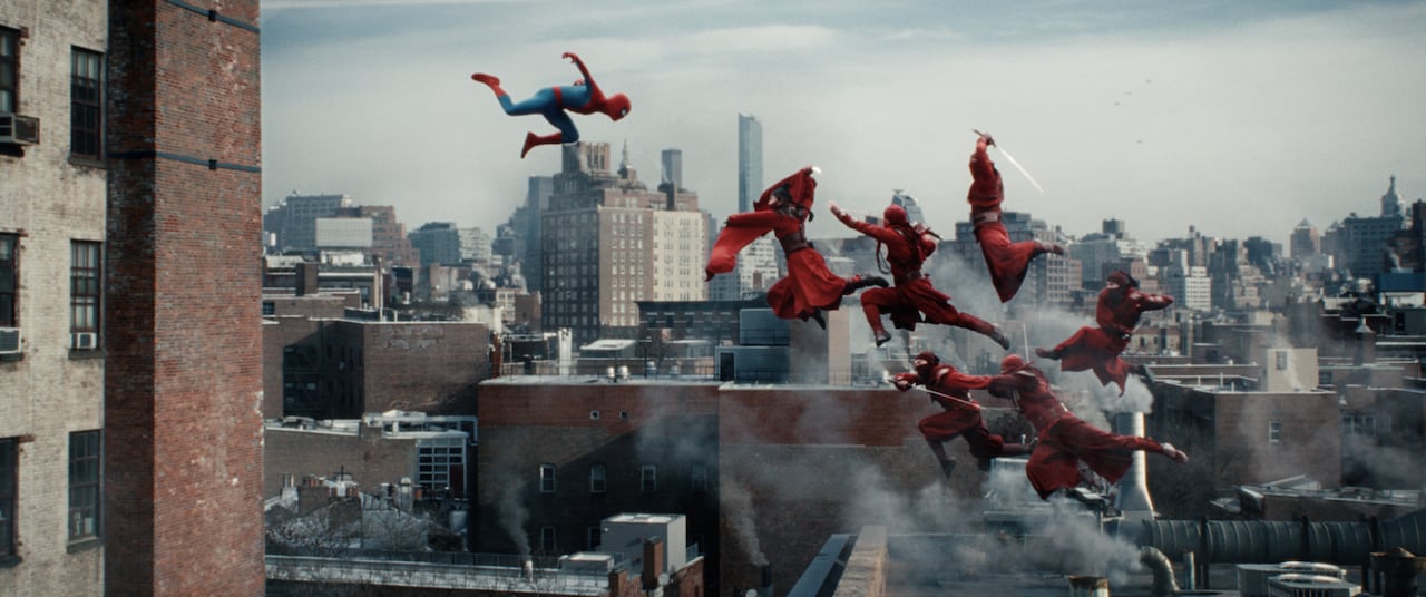 Spider-Man jumps off a building into a leaping group of ninjas.