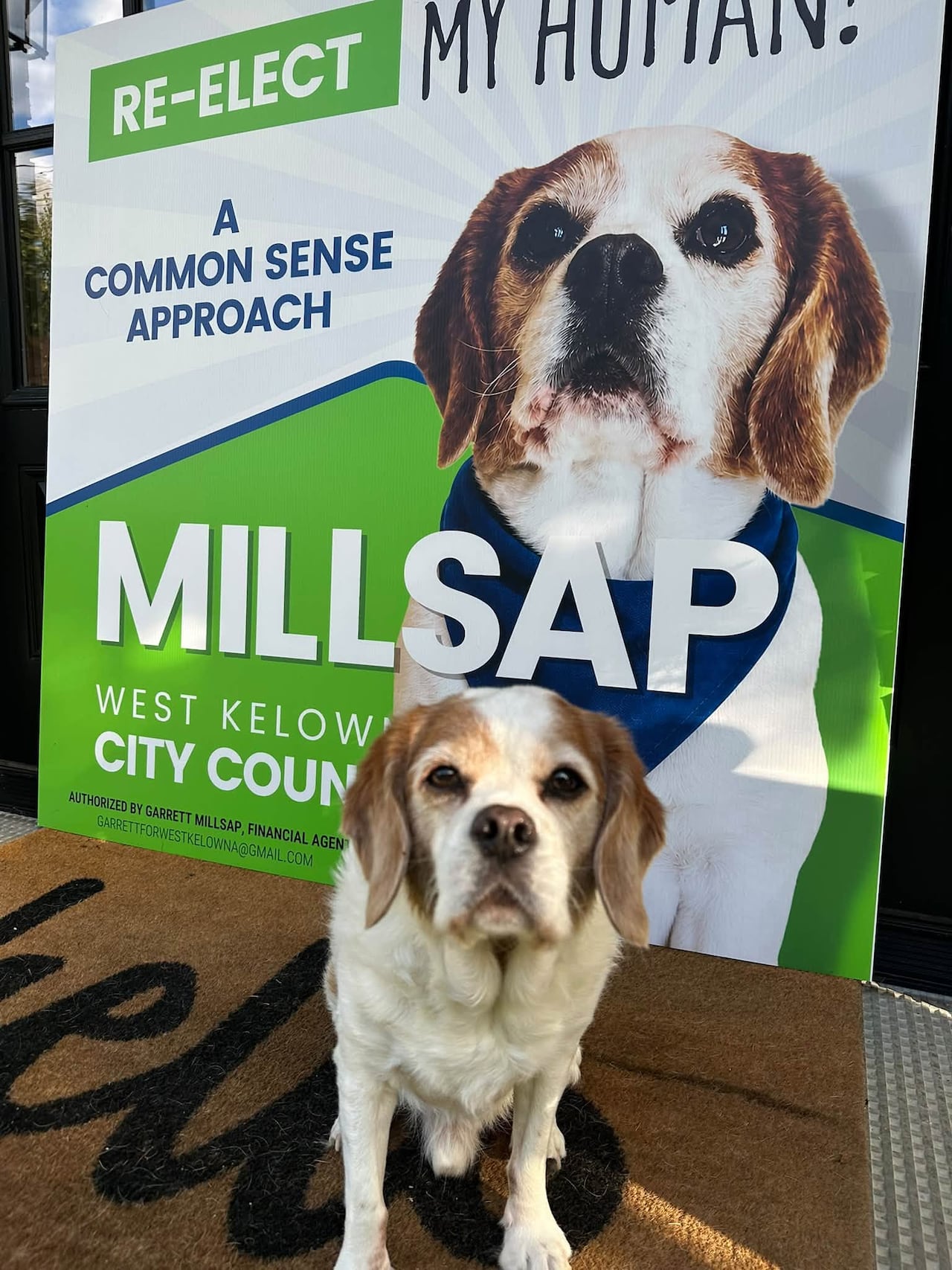A small dog standing in front of an election sign that features the same dog.