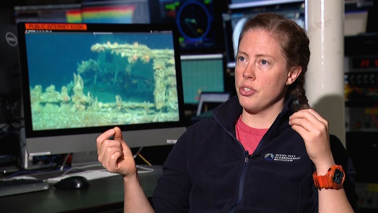 A woman sits at a desk with a computer screen showing an underwater image.