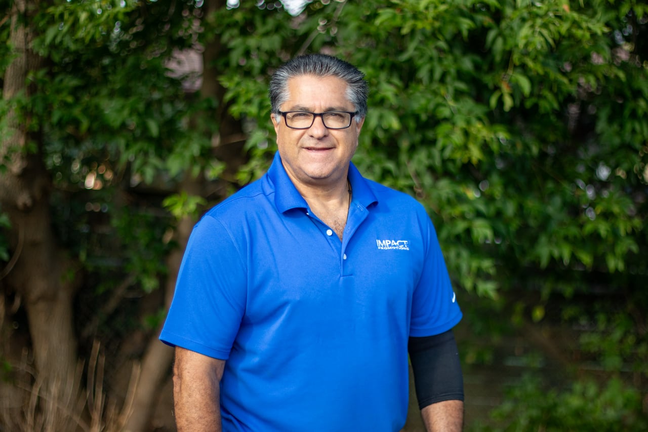 A person wearing a blue golf shirt and black arm sleeve stands outside.