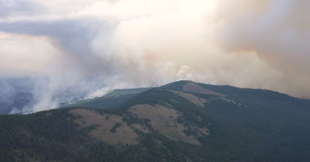 Smoke and clouds are billowing above a hilltop.