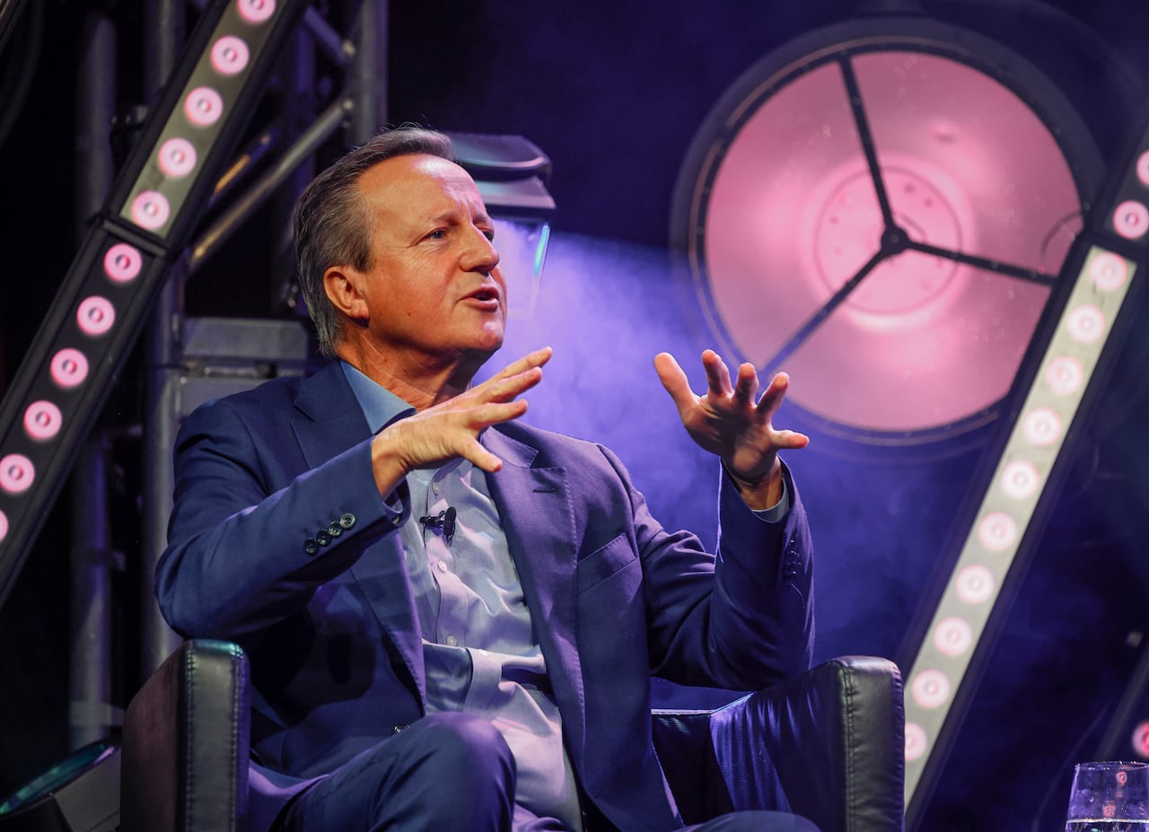 a white older man in blue suit sits in chair and talks and gesticulates