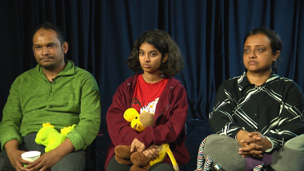 Man in green shirt sits next to daughter and wife holding stuffed animals.