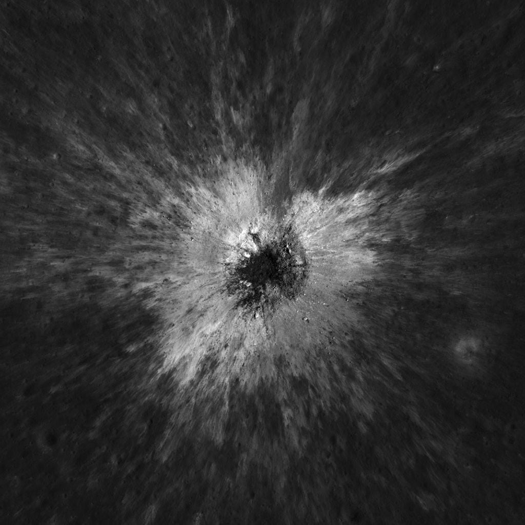 An overhead view shows a crater on the moon with bright ejecta surrounding it.