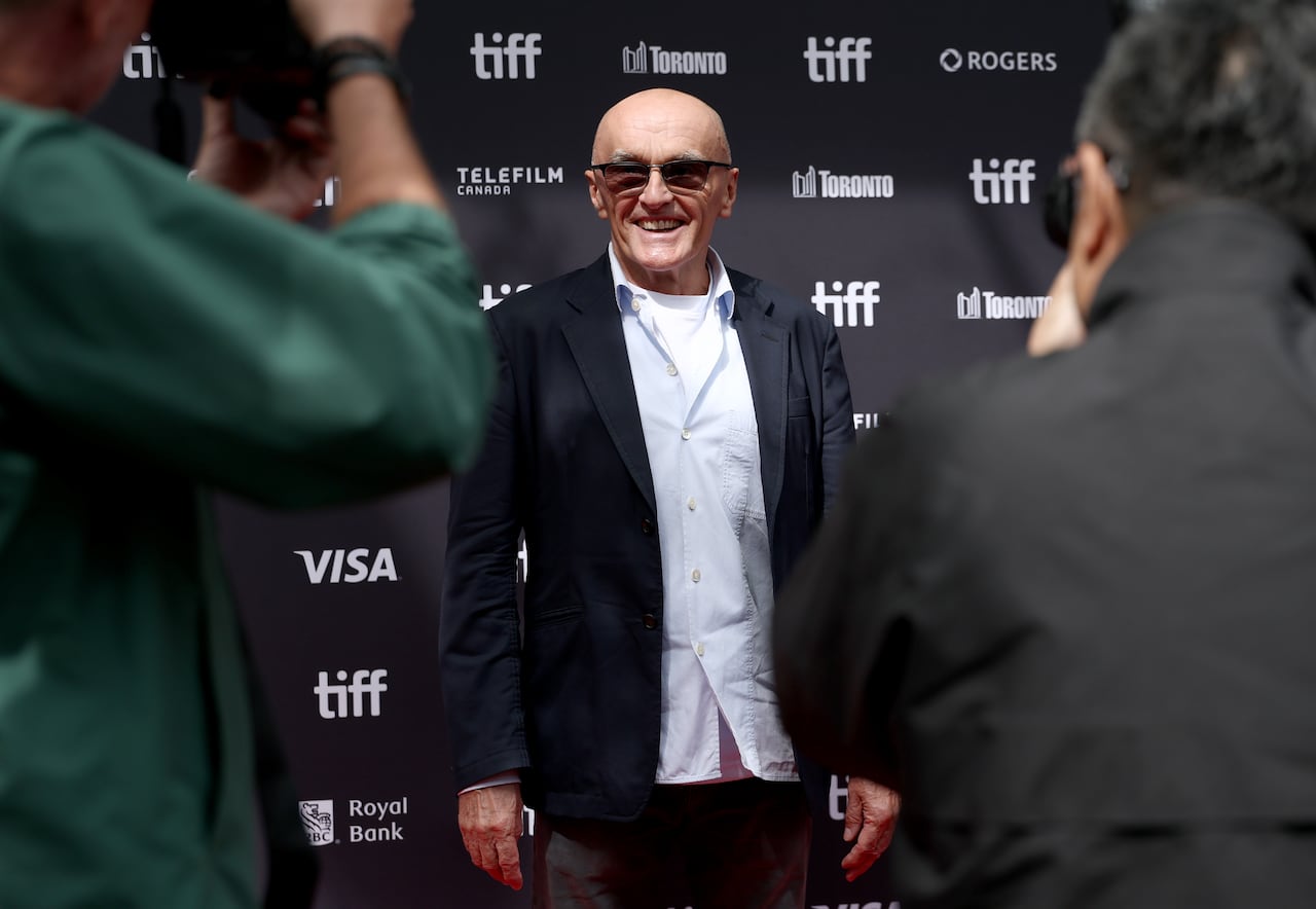 A man in open shirt and tuxedo jacket and pants having his photo taken by photographers on a red carpet.