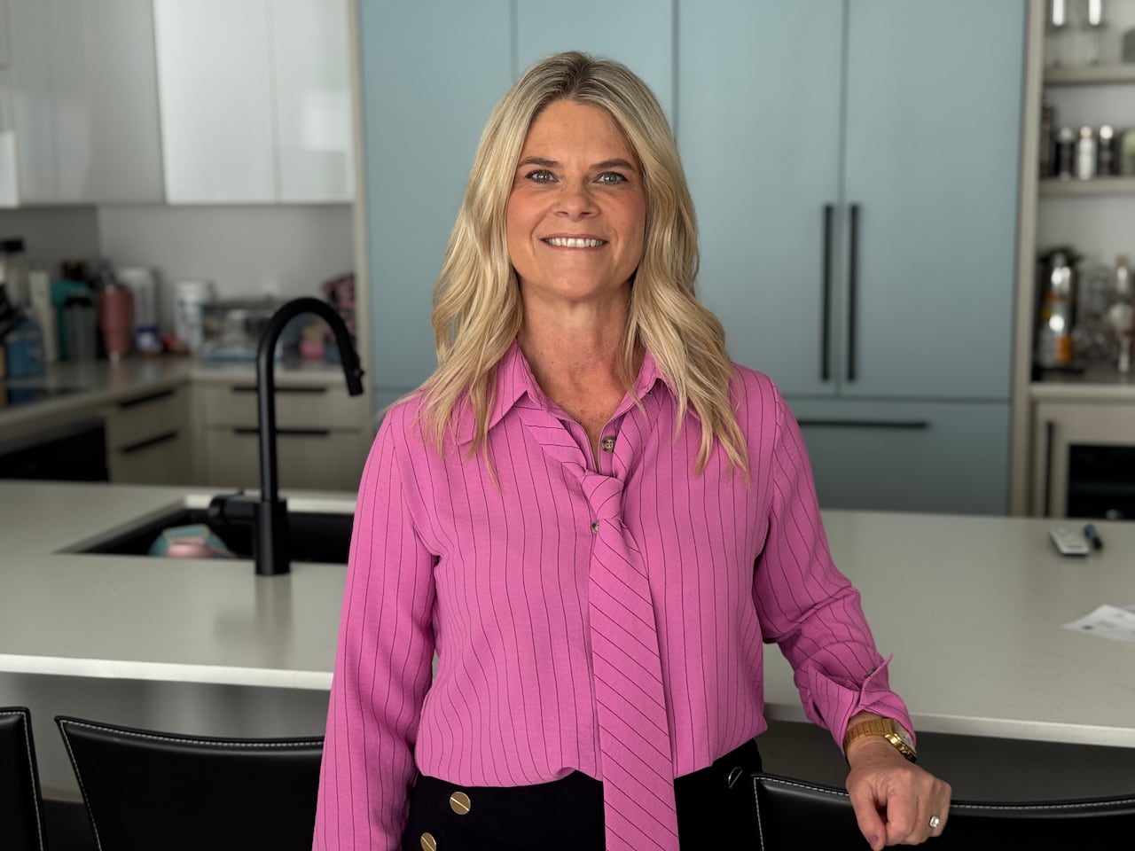 a blonde woman in a pink button up smiles for a photo in a condo kitchen