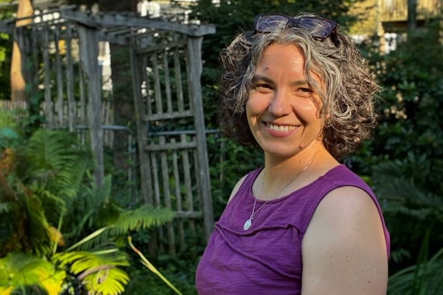 A woman in a purple top stands in a yard.