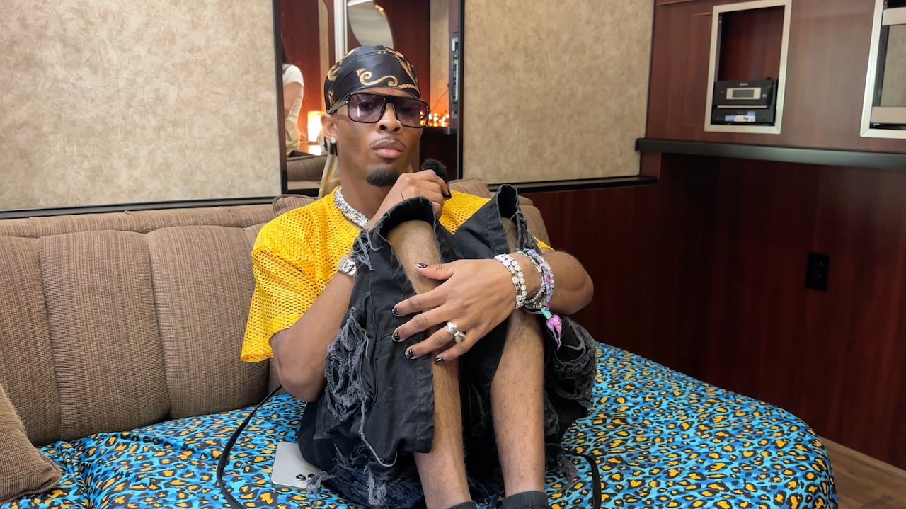 A man in a a bandana, a t-shirt and shorts sits on a couch.