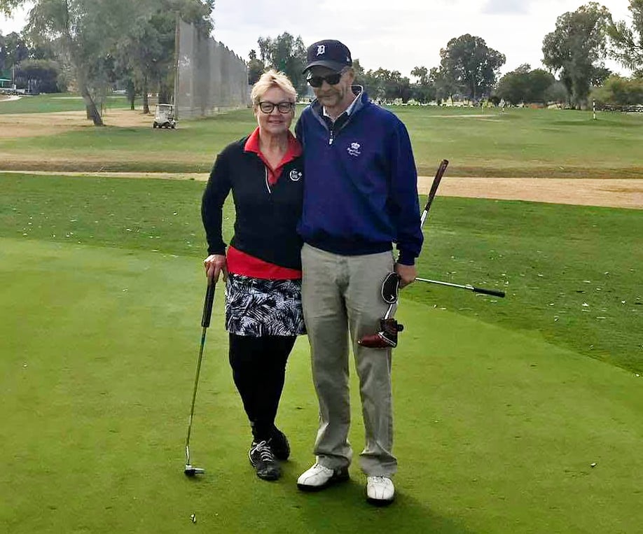 A man and woman stand on a golf course with gold clubs in their hands.