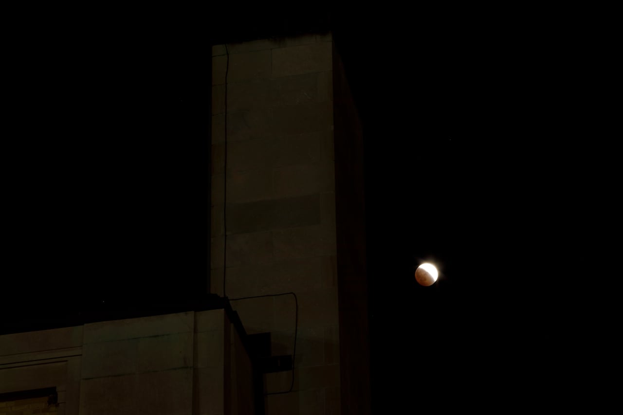 A partial lunar eclipse in the sky at night next a building.