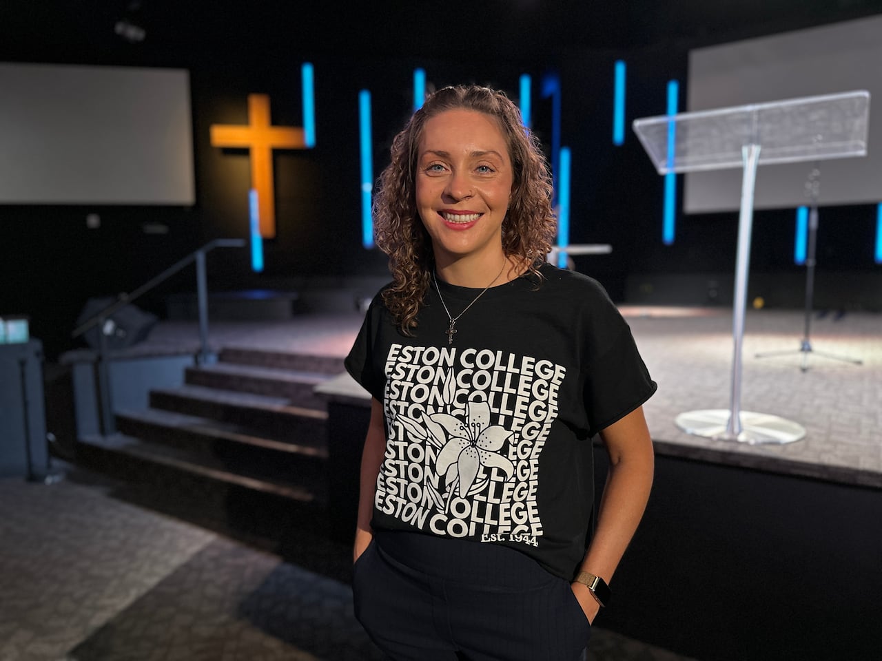 A woman stands for a photo in front of a stage in the sanctuary of a church.
