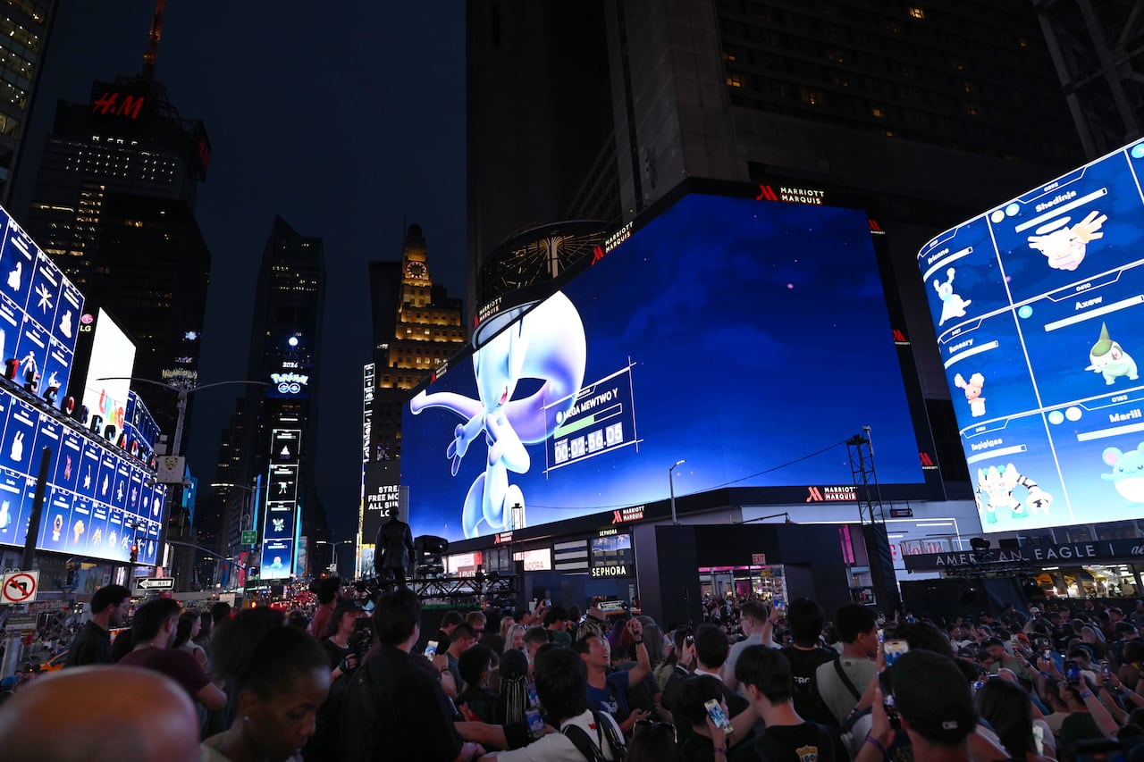 People pack Times Square at night, as images of Pokemon characters are shown on large screens.