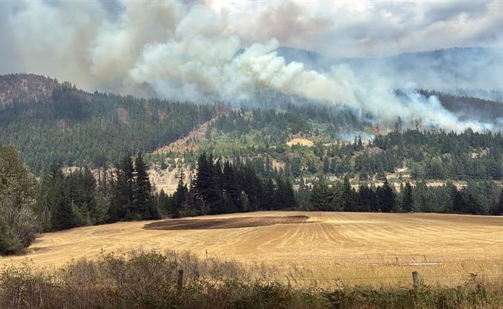 Smoke rises above a treed hill and dry field.