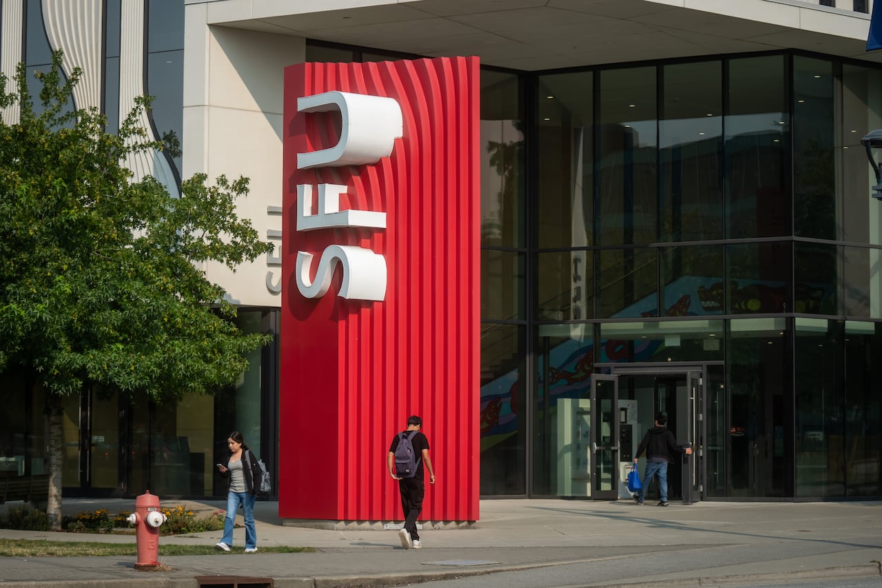 A university school building with a large red pillar in front of doors with a large "SFU" sign in white letters.