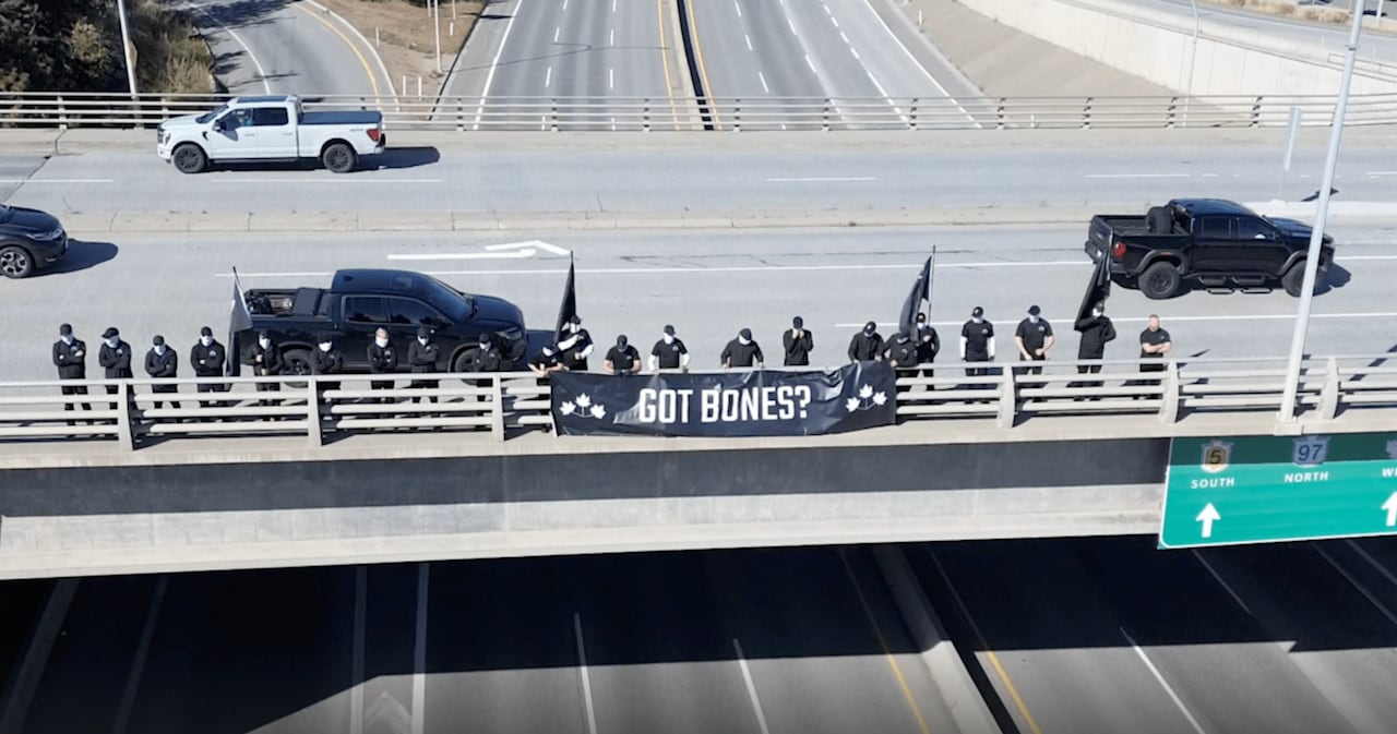 A group of masked men on a highway overpass.