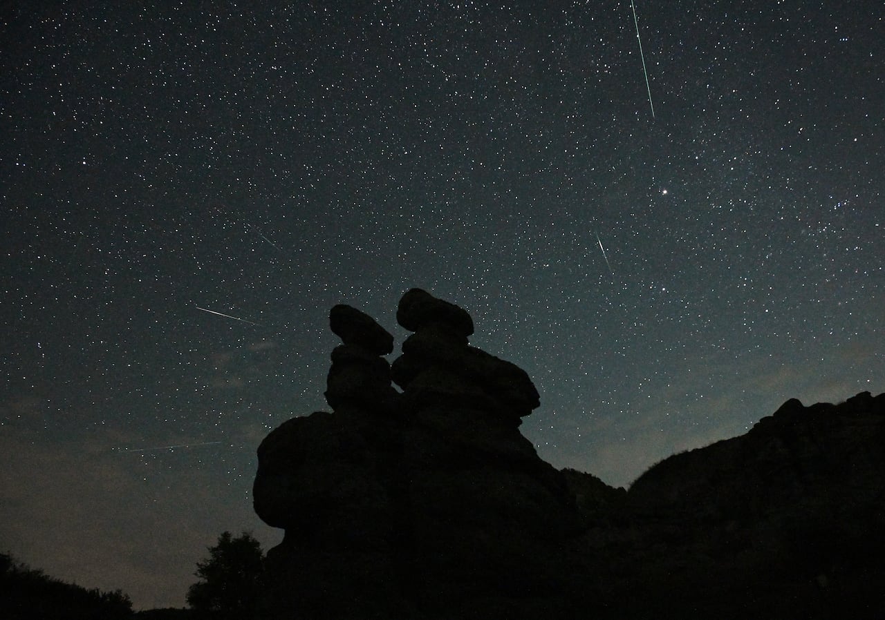 Rock formations in silhouette with meteor streaks and stars in the sky at night.