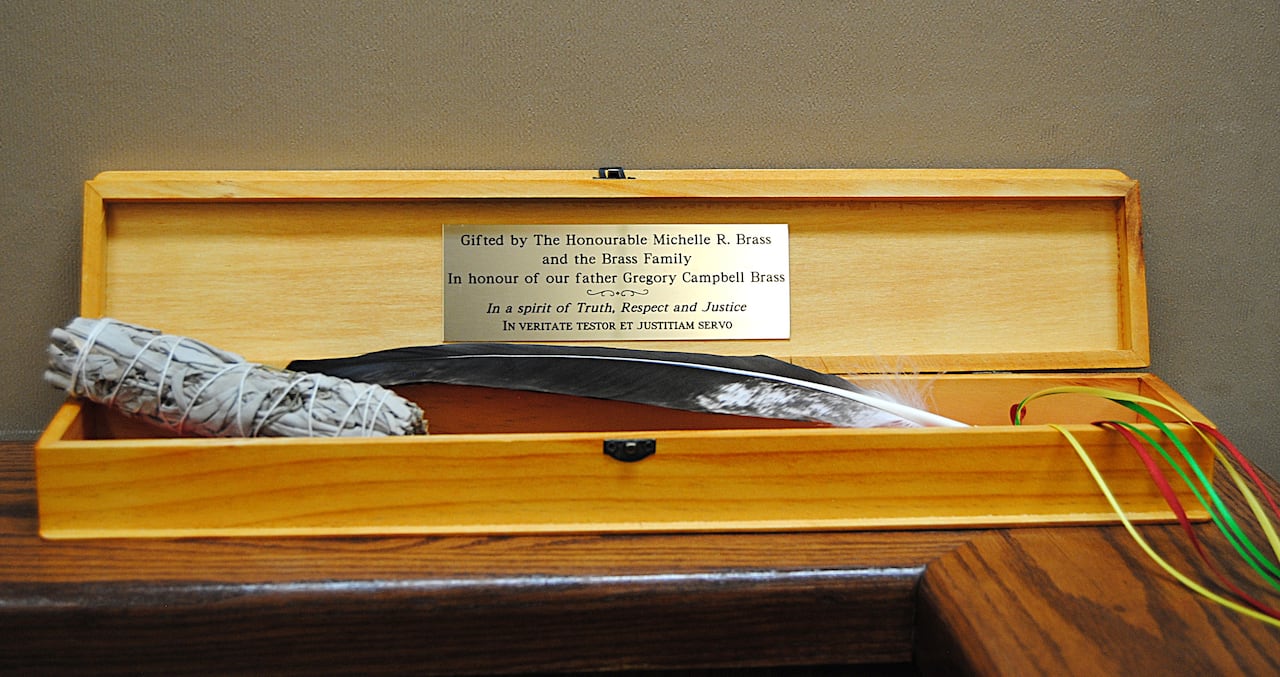 A feather and bundle of sage sit in a wooden box with a plaque reading \