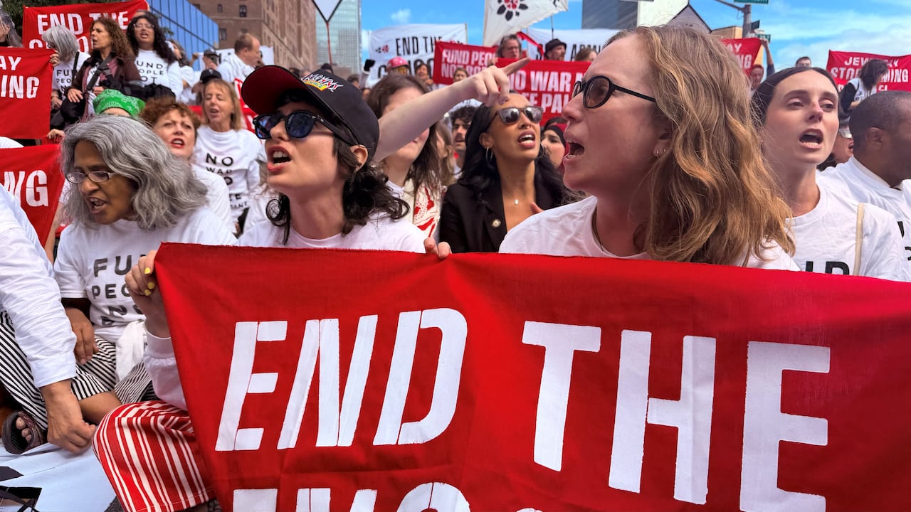 Two women hold a red banner at a protest.