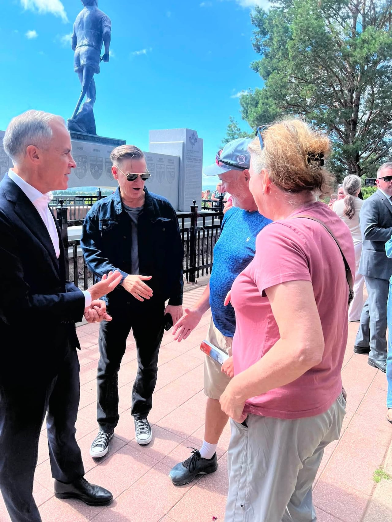 Prime Minister Mark Carney and musician Bryan Adams chat with the public in front of a statue of Terry Fox.