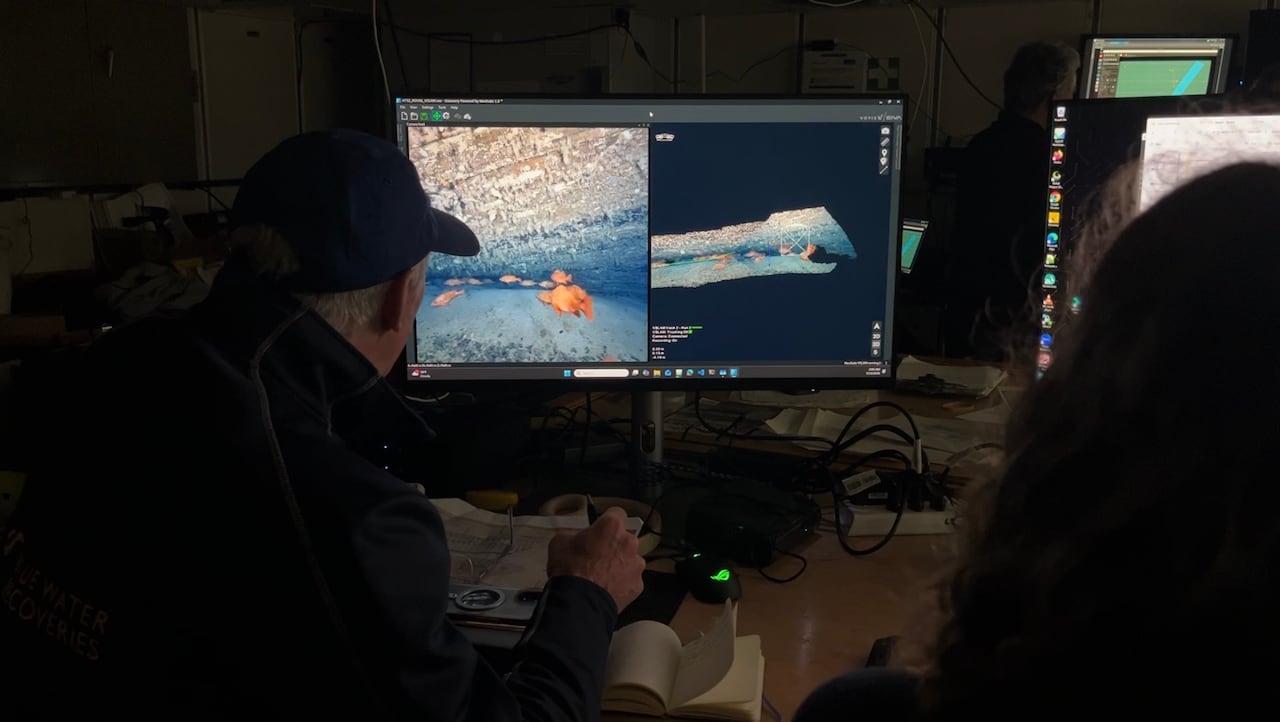 Two people look at a screen with underwater images on it.