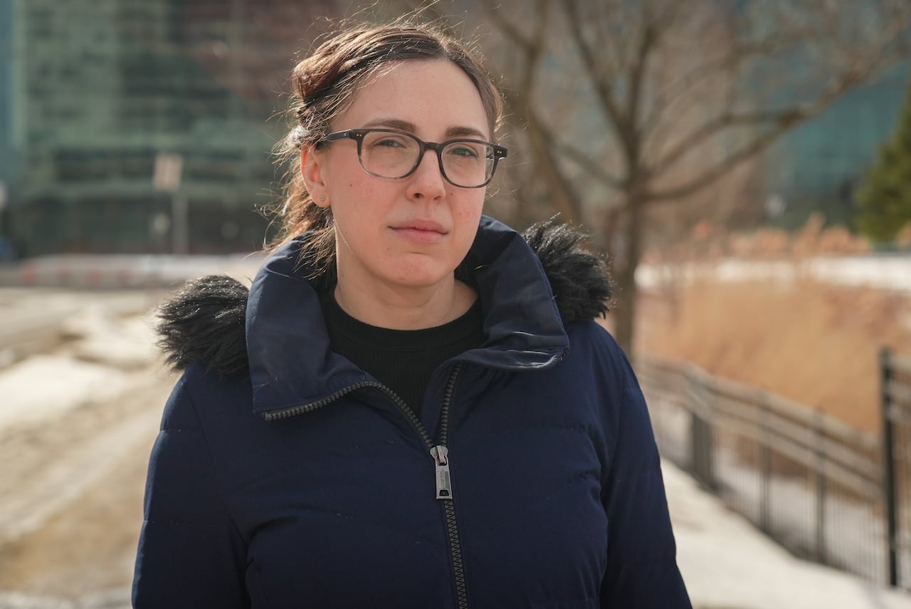 A woman in a winter jacket stands outside a building.