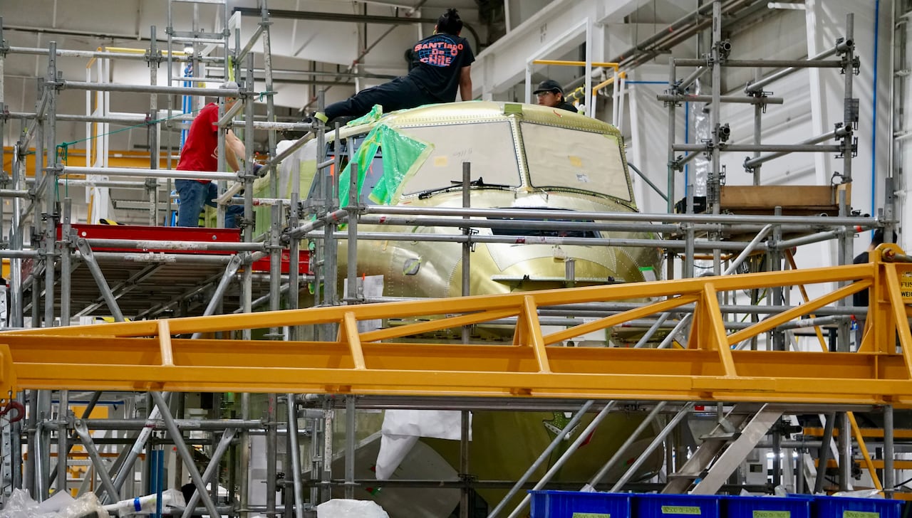 Workers and equipment are show around the green-coloured cockpit.