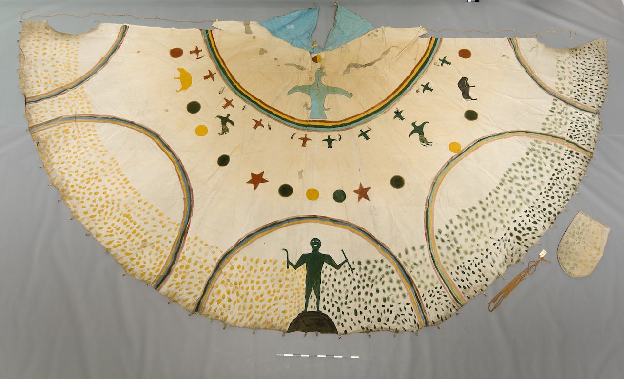 A painted teepee cover made of white hide, spread out over a grey surface.