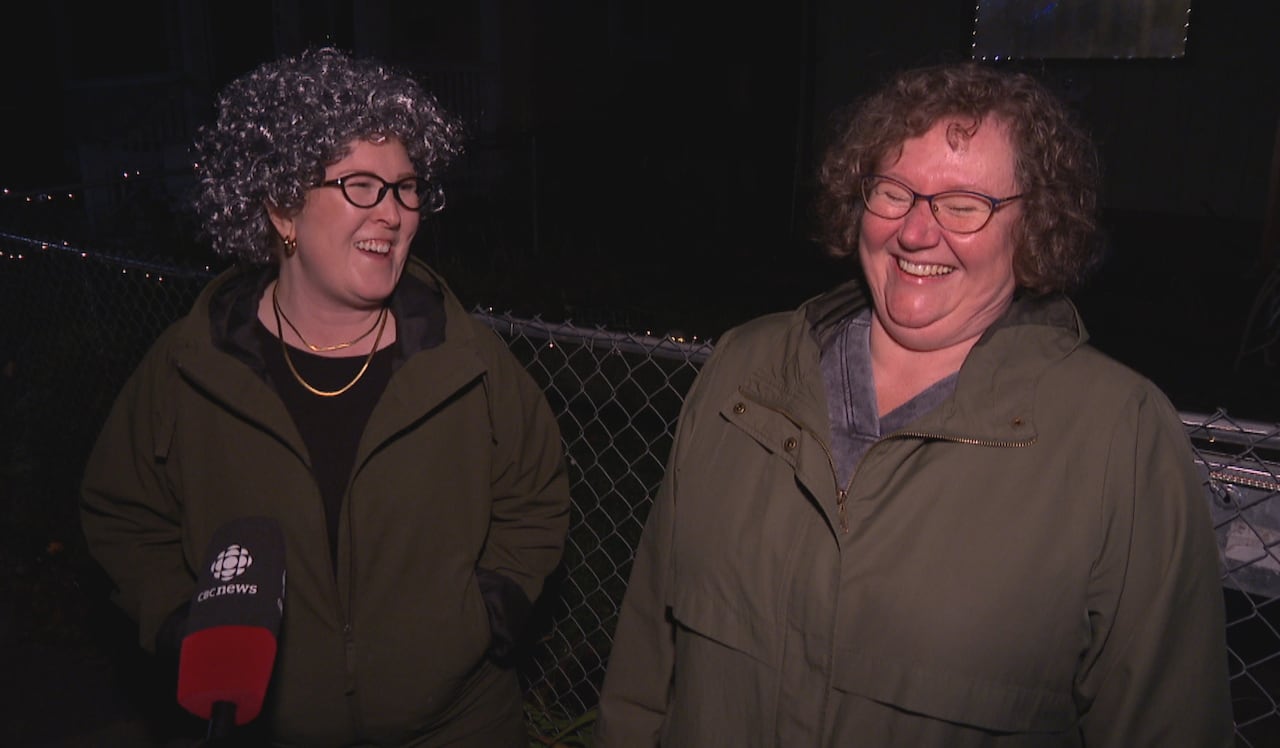 Two women, one dressed to look like the other, stand beside each other laughing.