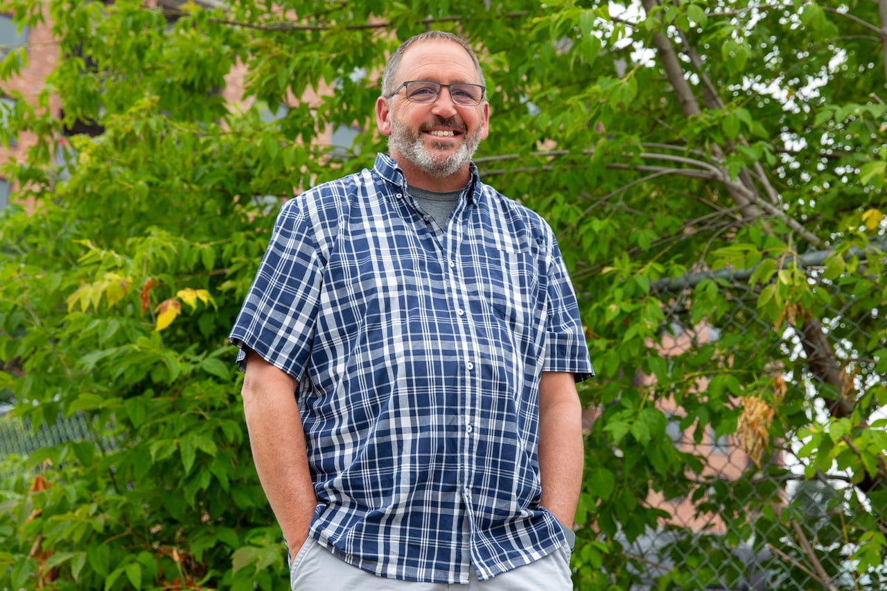 A person wearing a blue plaid shirt is seen standing outside.