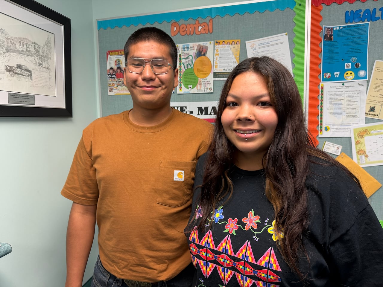 A young woman stands with her male partner in front of bulletin boards.