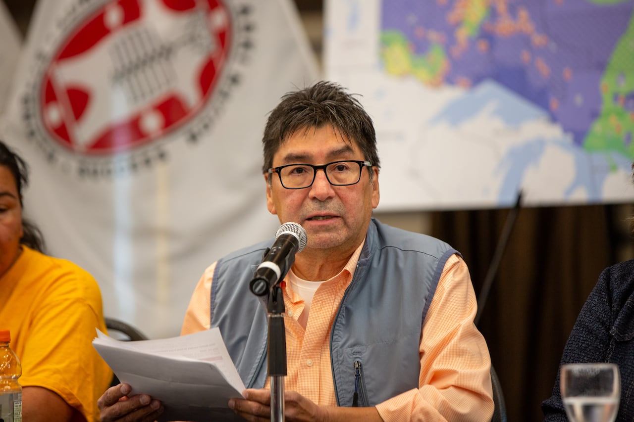 A person is seen speaking at a table with flags behind them.