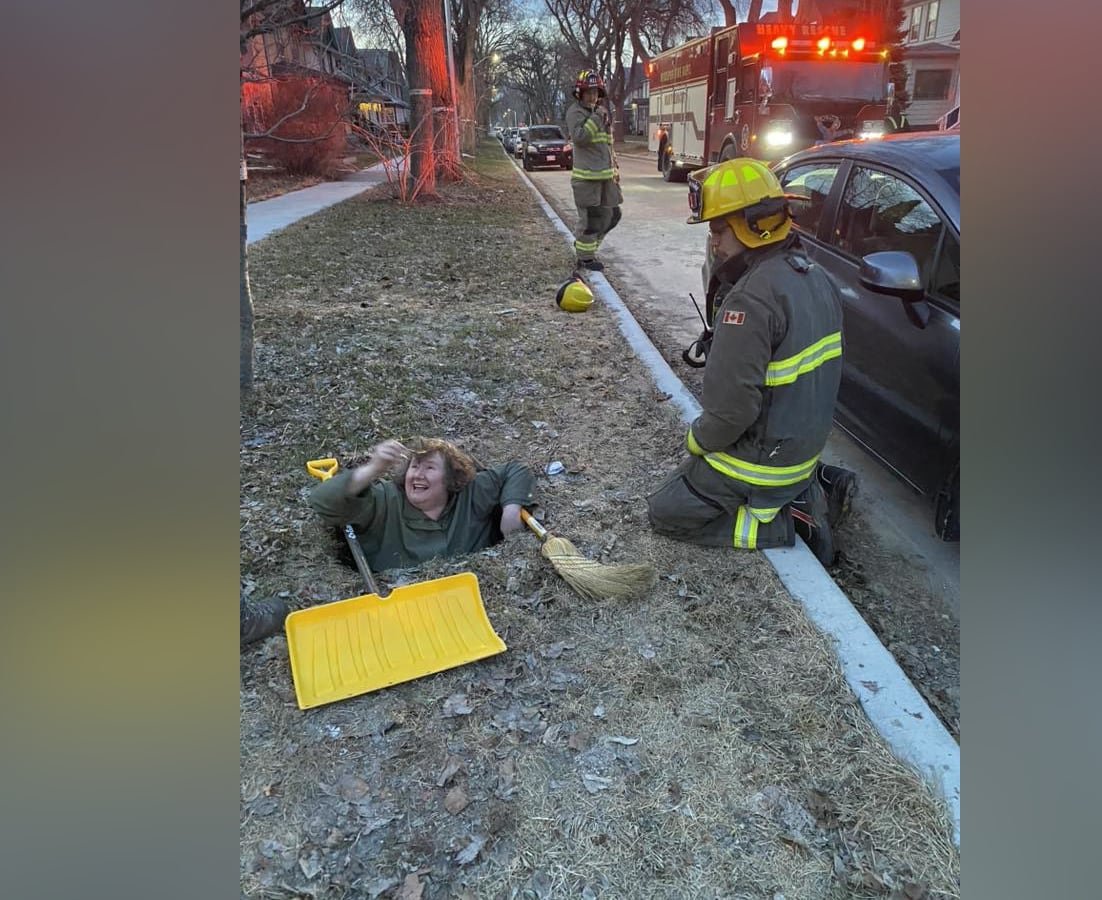 A woman is stuck in a hole on a grassy boulevard, up to her shoulders.
