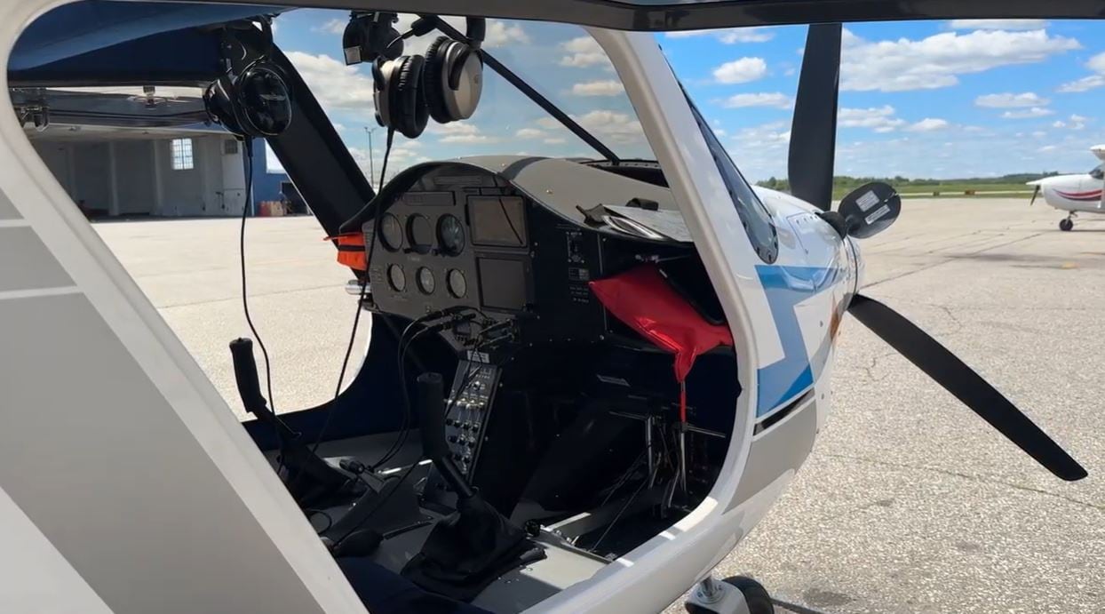 The exterior of a small, white aircraft with the doors open to see the controls inside.