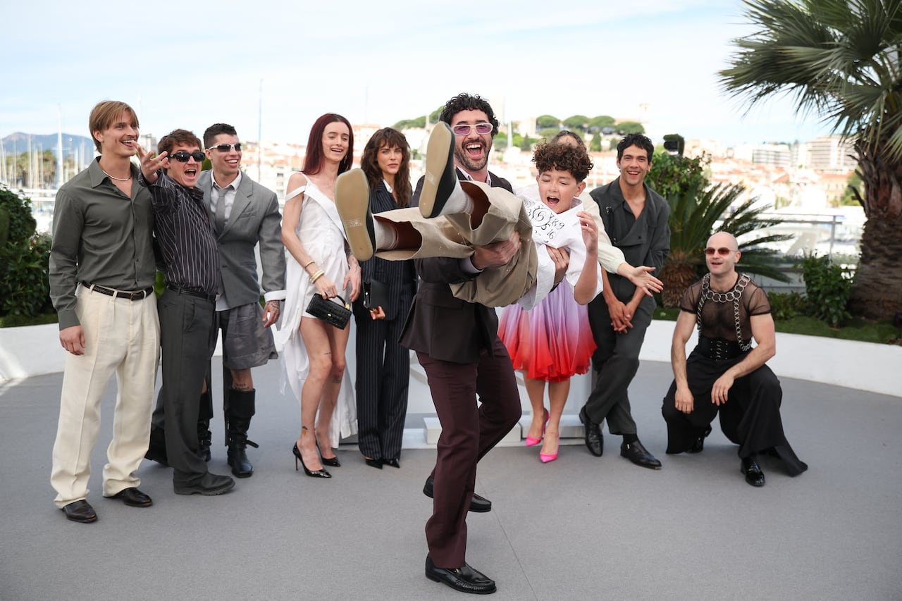 A smiling man picks a smiling boy off the ground. Behind them a number of people stand in a line, also smiling.