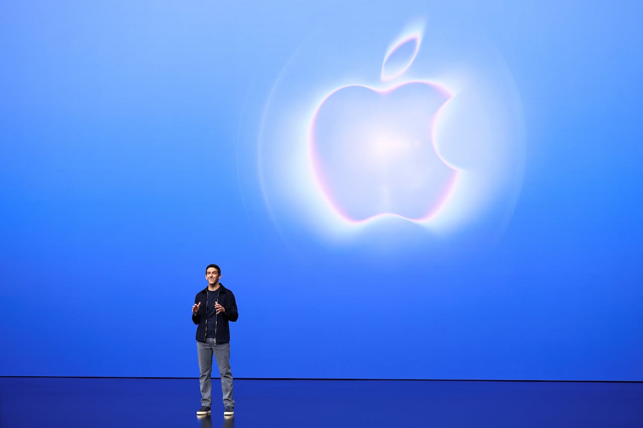 A man on a stage with a blue background behind him, and a white apple on the screen