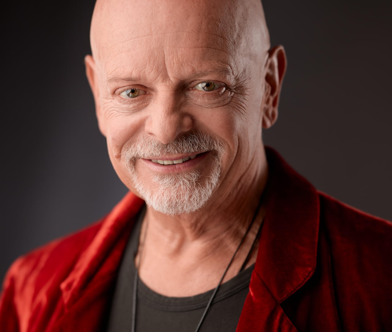 A smiling bald man in a black shirt and red jacket