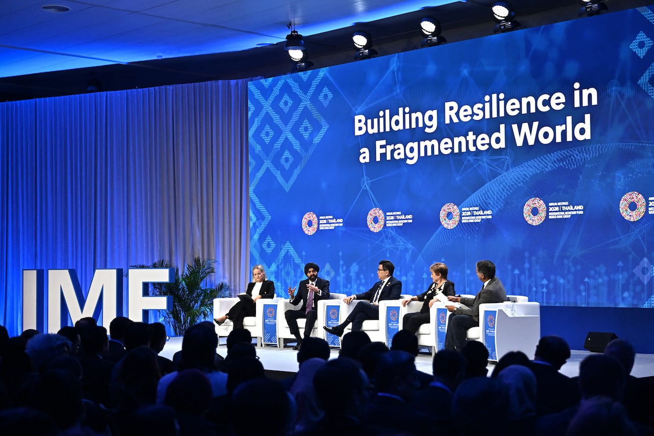 five people in suits sit on a stage engaging in a panel discussion