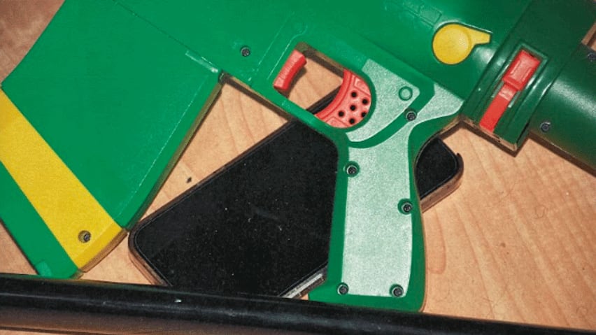 A closeup of a green plastic gun on top of a smartphone.
