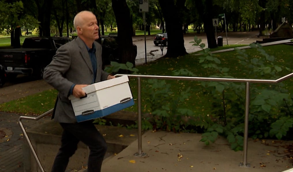 A man carrying a white cardboard file box walks up a set of concrete steps.