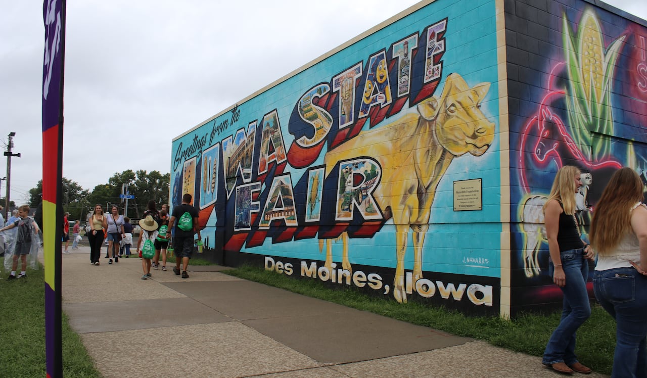 A colourful mural on the side of a building. The mural features a golden cow and the text "Greetings from the Iowa State Fair."