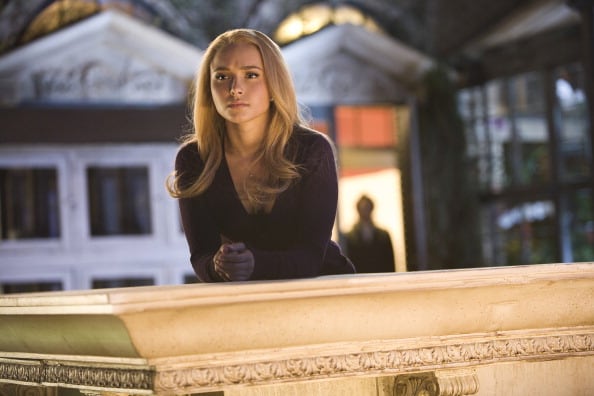 A young woman with blond hair stands near a ledge in a scene from a TV show.