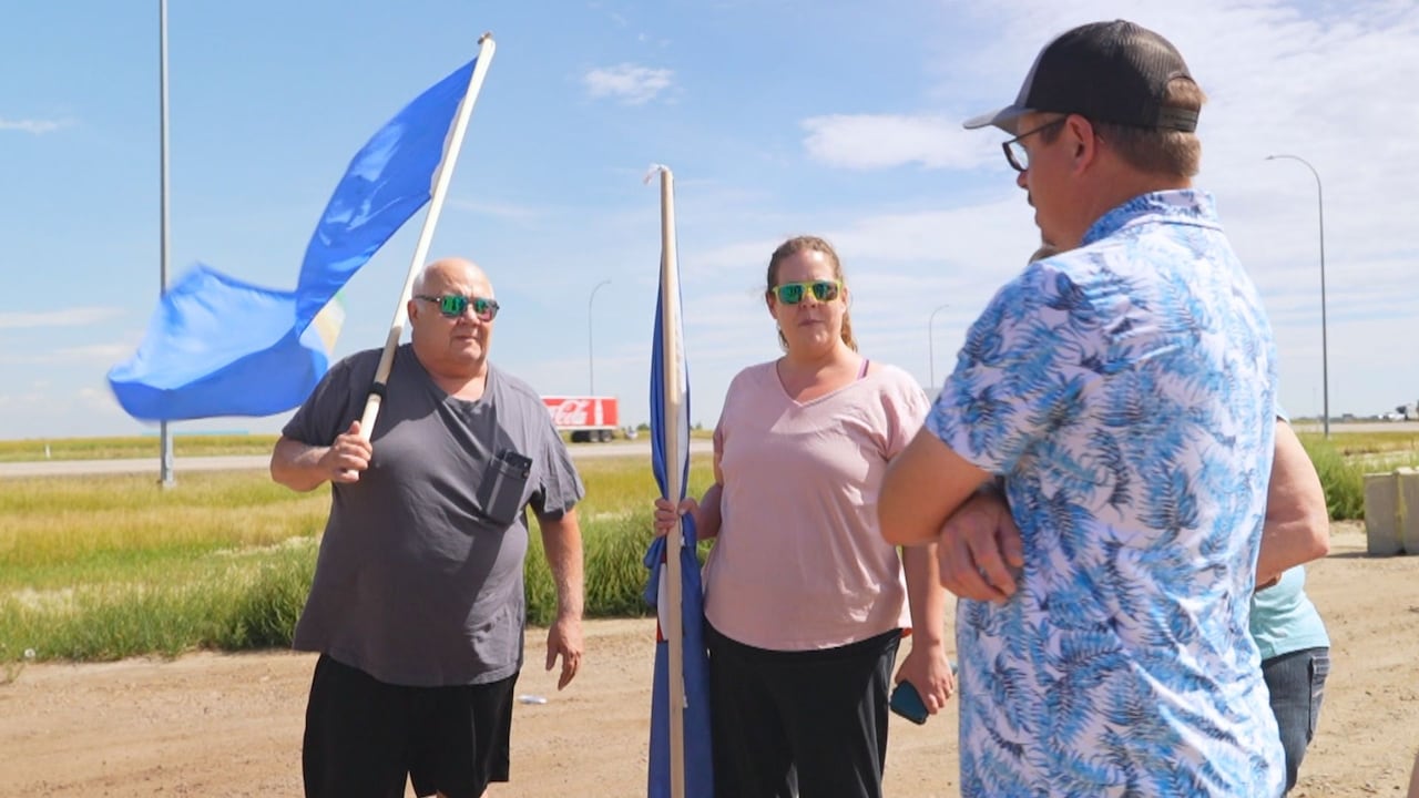 Three people gather and talk in a parking lot.