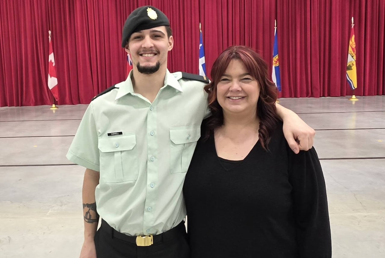 a man in uniform poses with his arm around a woman in an auditorium with flags
