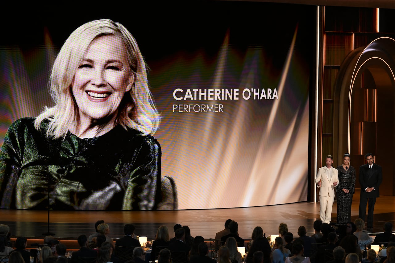 A large image of a woman on a screen with the words 'Catherine O'Hara' is shown next to three standing figures.