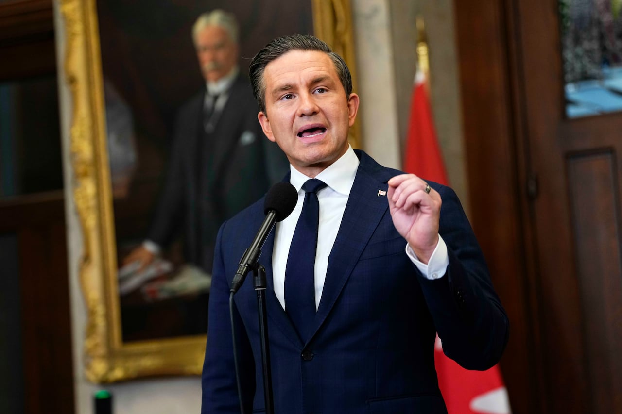 A man in a suit gestures with his hand while he speaks into a microphone.