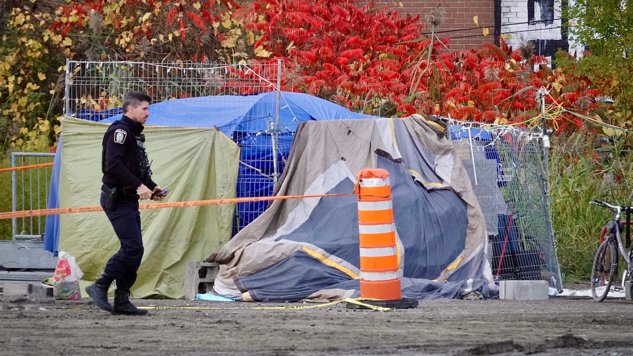 police officer walks past a homeless encampment