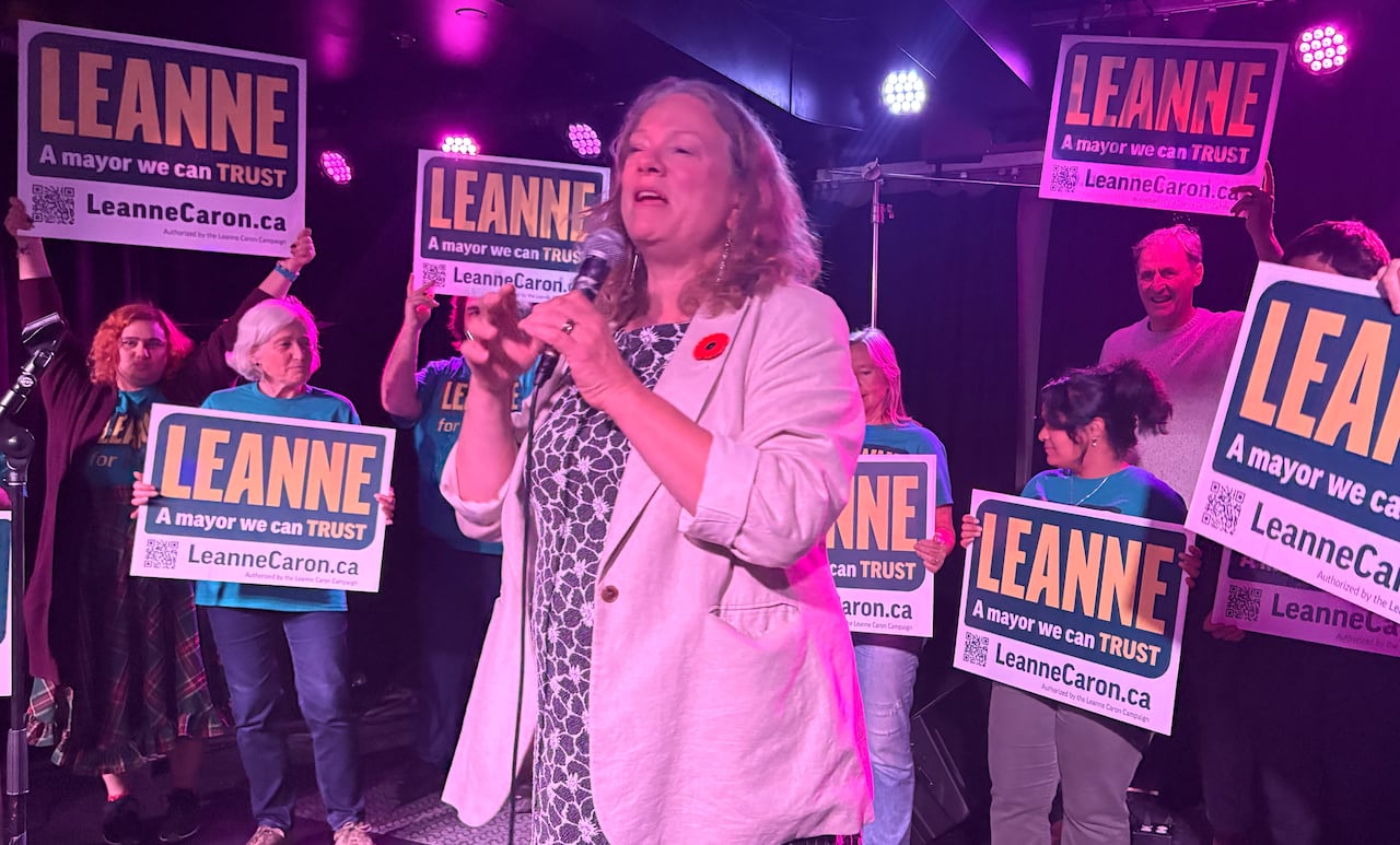 Woman with microphone speaks to crowd as they hold up campaign signs behind her