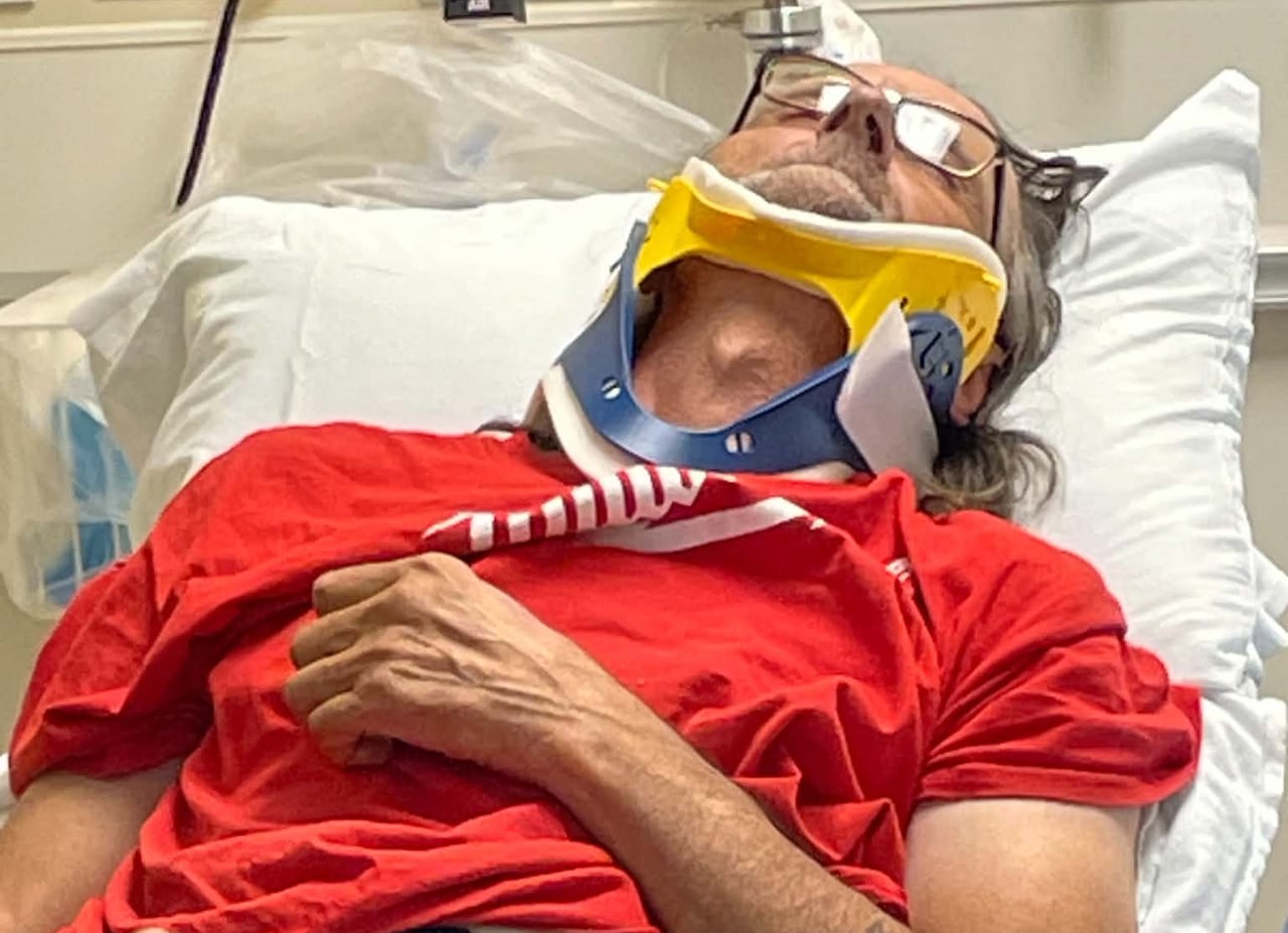 A man lies down in a hospital bed with a medical device on his neck.